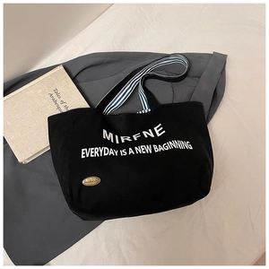 Detail of black canvas tote with white lettering and striped woven handle on white bedding