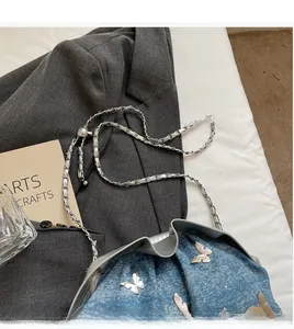 Detail of blue denim bucket bag with silver butterfly charm and chain strap