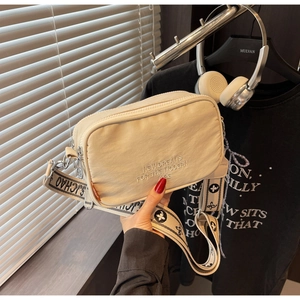 Detail of cream nylon crossbody camera bag featuring letter embroidery and wide strap