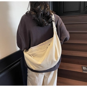 Back view of a large cream canvas crescent bag with wide strap on a female model