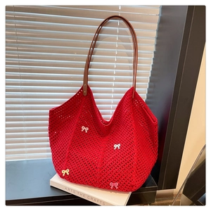 Detail of red crochet tote bag with colorful bows and brown leather handles on a book