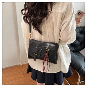 Detail of a vintage black saddle bag with white stitching and gold hardware on a leather strap