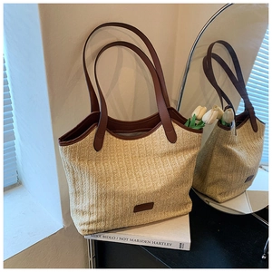 Detail of straw tote bag with brown leather handles placed on books in soft sunlight