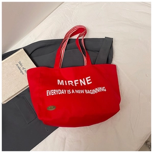 Detail of red canvas tote bag with letter print and striped handles on a coat