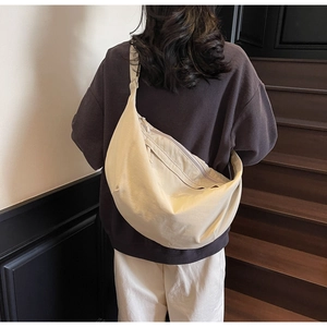 Detailed back view of a beige crescent crossbody bag worn by a model on wooden stairs
