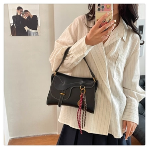 Detail of black leather saddle bag with white contrast stitching and woven charm