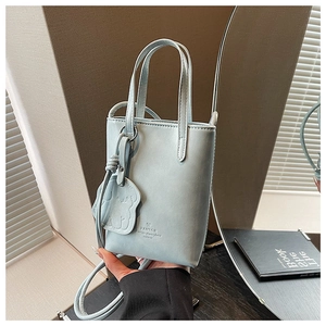 Detail of light blue mini bucket bag featuring a matte leather texture and cute bear charm