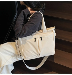 Detail of cream canvas tote bag featuring dual front zipper pockets and adjustable straps