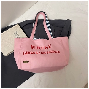 Close-up of pink canvas tote bag with red lettering and blue striped inner strap