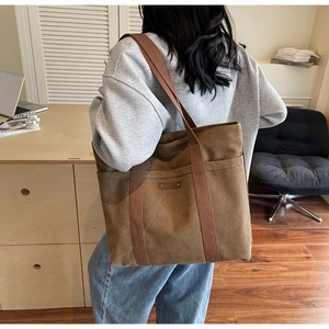 Close-up of wide straps on a large tan canvas tote bag worn by a model in a cozy room