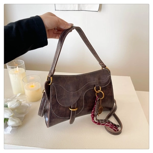 Detailed view of dark brown saddle bag with contrast stitching and woven rope charm