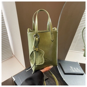 Green mini tote bag with dog charm and crossbody strap on a lifestyle background