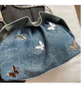 Detail of blue denim cloud bag with silver butterfly charms and chain strap