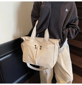 Detail of a beige multi-pocket tote bag with adjustable strap shown on a casual model