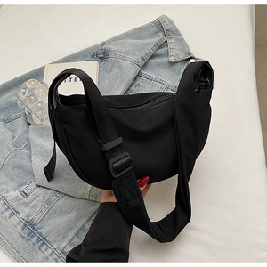 Close-up of black crescent nylon crossbody bag with wide shoulder strap on bed