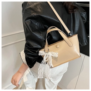 Dettaglio borsa a secchiello beige con ciondolo a fiocco di perle su modella di spalle