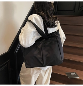 Detailed view of black nylon tote bag with dual zipper pockets and silver ring pulls