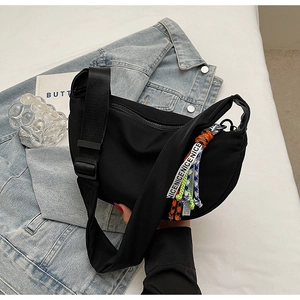 Detail of black nylon half-moon crossbody bag with colorful braided tag on denim jacket