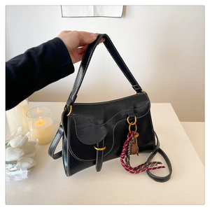Detail of black leather saddle bag with white contrast stitching and a fringe pendant