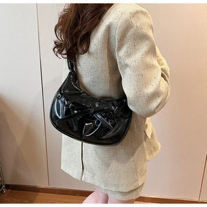 Vue latérale d'un sac à bandoulière en cuir verni noir avec nœud sur mannequin