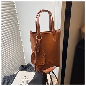 Detailed shot of brown mini tote bag featuring cute bear charm and logo embossing