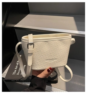 Detailed macro view of white woven texture leather and metallic strap buckle on bucket bag