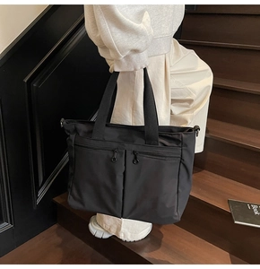 Detail of black nylon tote bag showing dual front zipper pockets and sturdy carry handles
