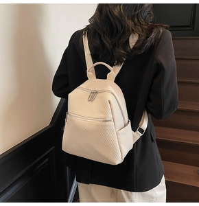 Detail of cream backpack showing diagonal woven texture and multi-layer zipper pockets