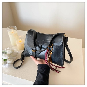 Detail of a vintage black saddle bag with white contrast stitching and tassel charm
