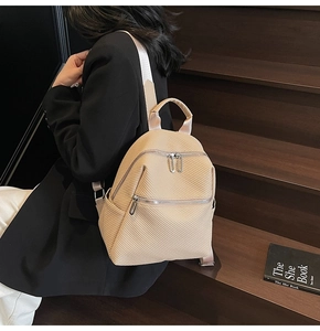 Detailed texture of beige woven backpack with silver zippers and webbing shoulder straps