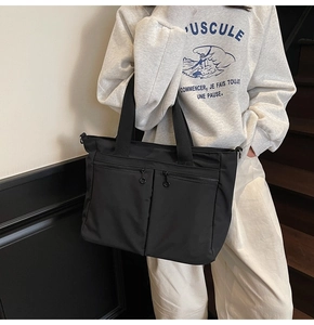Detail of black nylon tote bag featuring dual front zipper pockets and durable handles