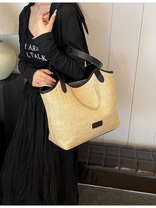 Minimalist beige woven tote bag with black handles shown as a stylish shoulder bag on model