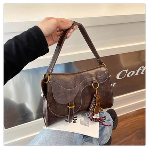 Close-up of vintage dark brown leather saddle bag with contrast stitching and decorative charms