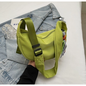 Detail of light green half-moon nylon bag with wide strap on denim jacket