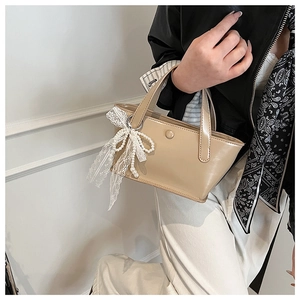 Dettaglio della borsa in pelle beige con fiocco in pizzo decorativo e ciondolo di perle