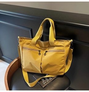 Detailed view of yellow canvas tote bag with front dual zipper pockets on a chair