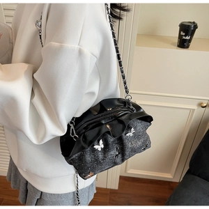 Detail of black bucket bag featuring pleated opening and white butterfly charm decoration