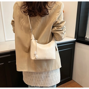 Detail der cremefarbenen Dumpling-Tasche mit Perlenfransen an einem beigen Blazer