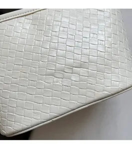Close-up of white woven leather bag detail featuring embossed brand logo and texture