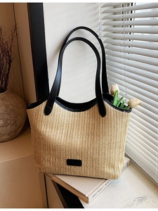 Large beige woven straw tote bag with black leather straps and fashion label on a windowsill