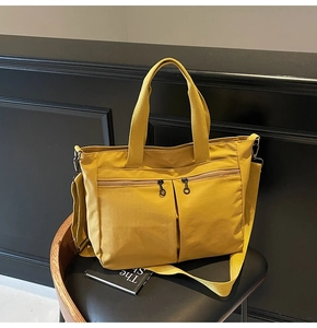 Detail of ginger yellow canvas tote bag with dual front zippers on a black leather chair
