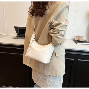 Weiße glänzende Leder-Hobo-Tasche mit Kugelanhänger an der Schulter des Models gezeigt
