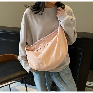 Detailed side view of a large light pink crescent crossbody bag worn by a model