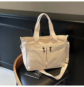 Detail of off-white canvas tote bag featuring double front zip pockets and adjustable strap