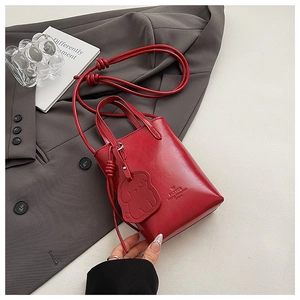 Detail of a red patent mini tote bag with bear charm on a grey blazer background