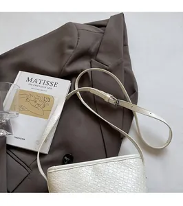 Detail of white woven underarm bag featuring an adjustable shoulder strap and soft leather