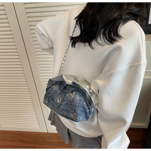 Detail view of a blue denim bucket bag with silver butterfly accents and chain strap