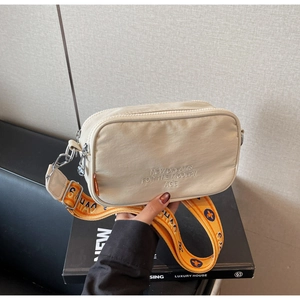 Detail of beige canvas crossbody bag with orange jacquard strap and embroidered text