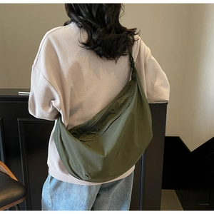 Detail of a dark olive green nylon dumpling bag worn as a crossbody for travel and commuting