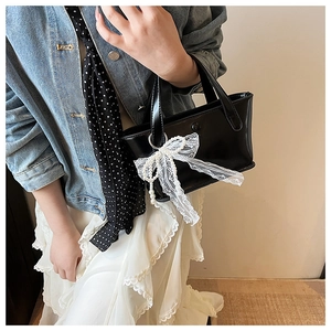 Dettaglio borsa nera lucida con fiocco in pizzo e catena di perle su denim